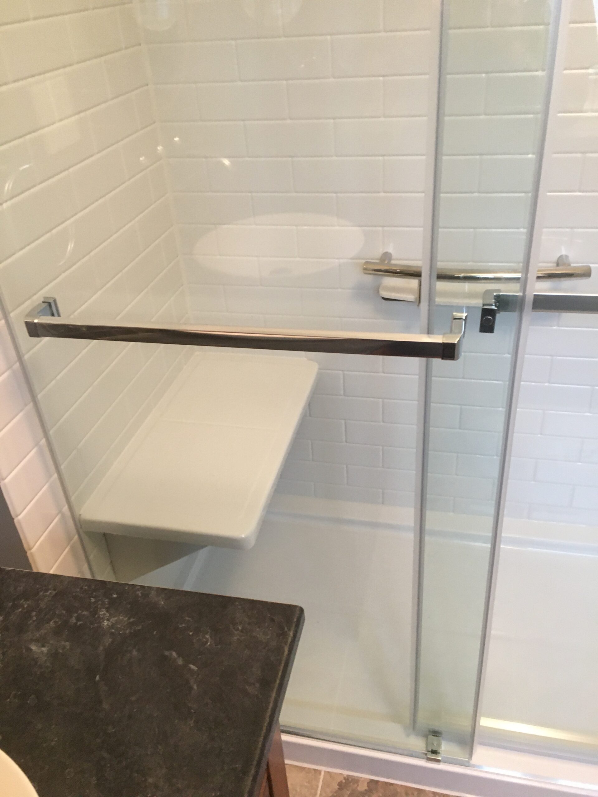 Built-in shower seat in an acrylic shower mimicking subway tile after remodeling.