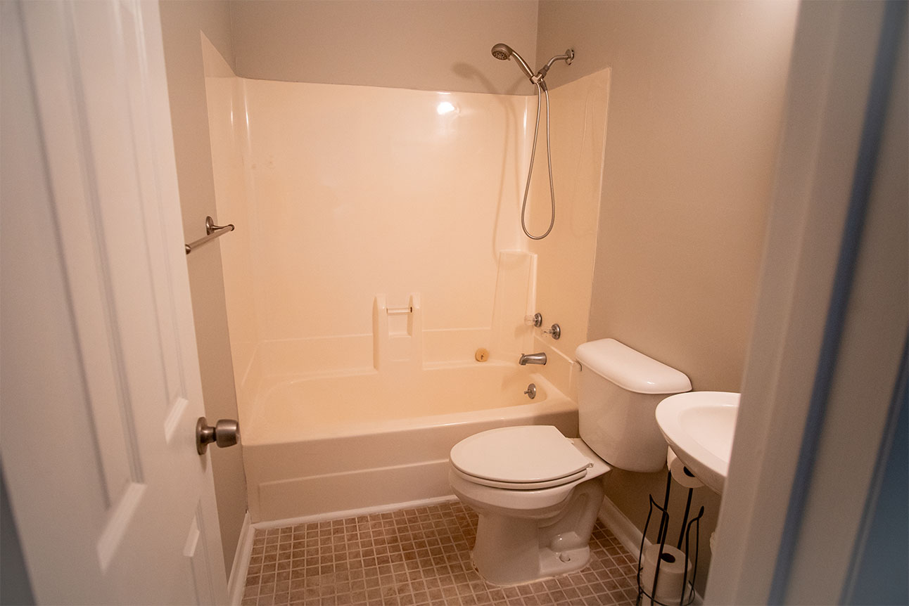 Before picture of a dated bathroom with a tub, old fixtures, and beige tiles.