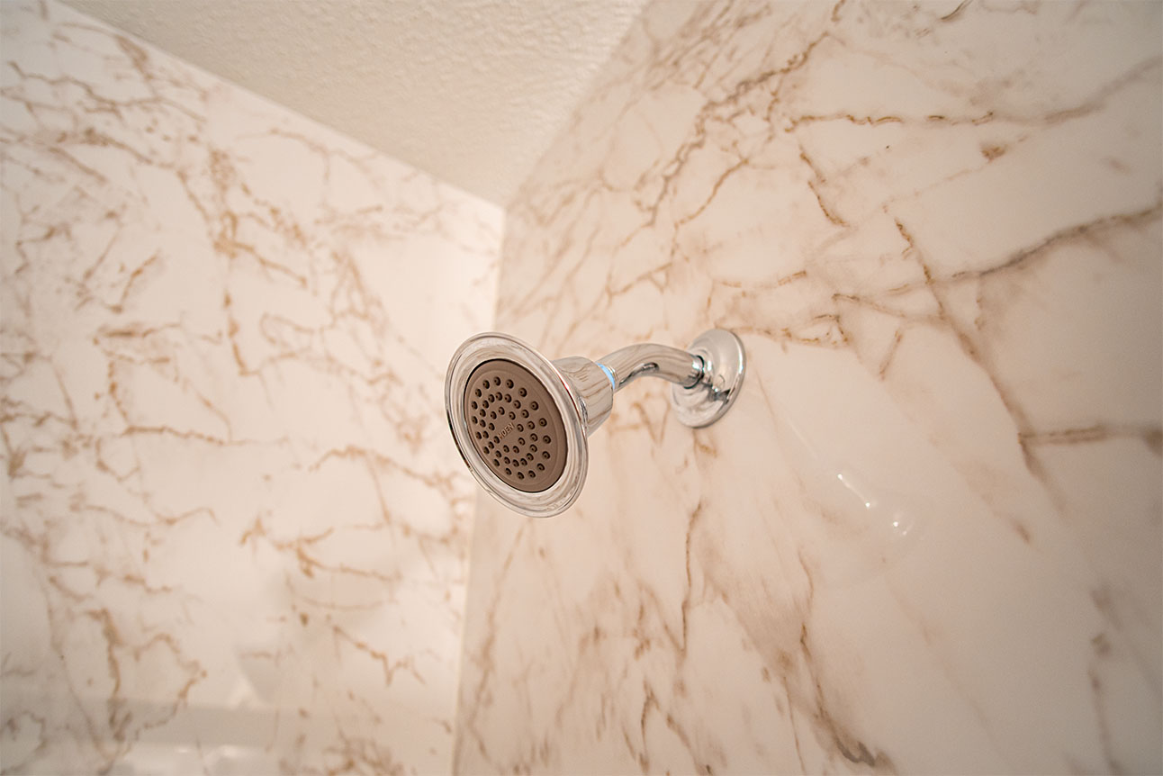 Close-up of a modern shower head in a marble-patterned shower.
