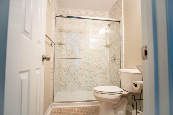Bathroom with a newly converted tub to shower, featuring elegant marble-patterned walls and a glass shower door.