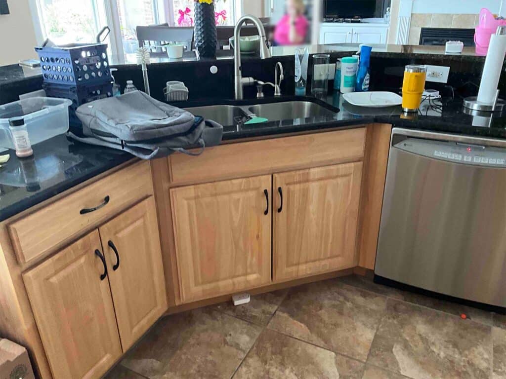 Before image of a kitchen showcasing the sink area with dated orange cabinets