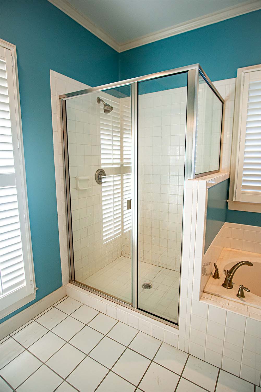 Before image of a moldy white tile shower with dated glass doors.