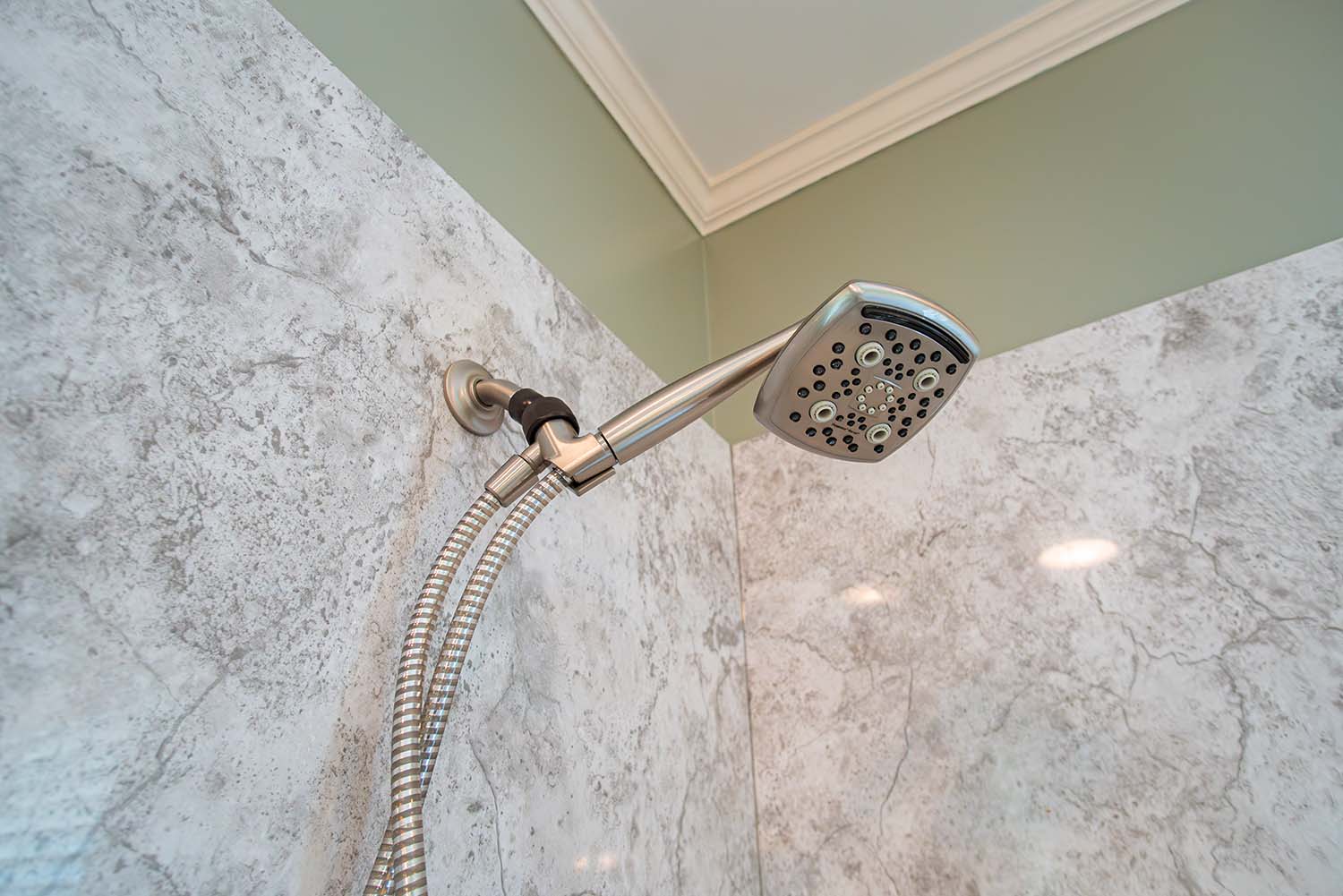 After image of the shower head area, featuring a handheld shower in a remodeled shower with granite-style acrylic walls.