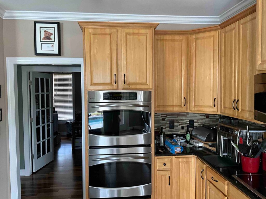 Before image of a kitchen showcasing the double oven area with dated orange cabinets