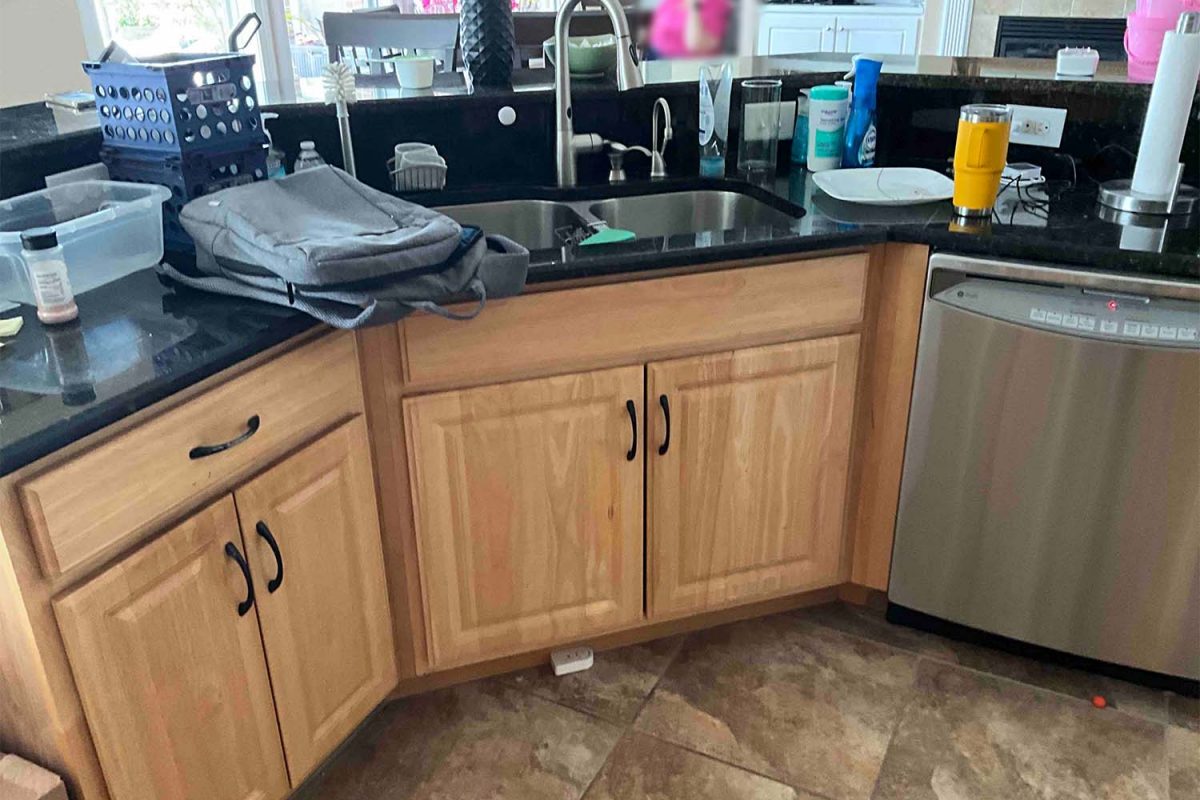 Before image of a kitchen showcasing the sink area with dated orange cabinets