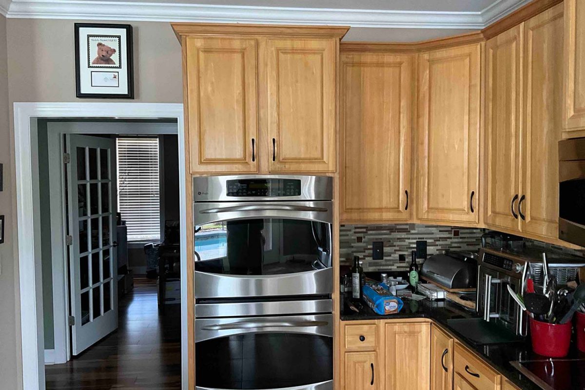 Before image of a kitchen showcasing the double oven area with dated orange cabinets